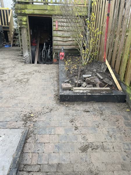 Dezelfde achtertuin na de werkzaamheden met nieuwe klinkerbestrating en border met zwarte rand