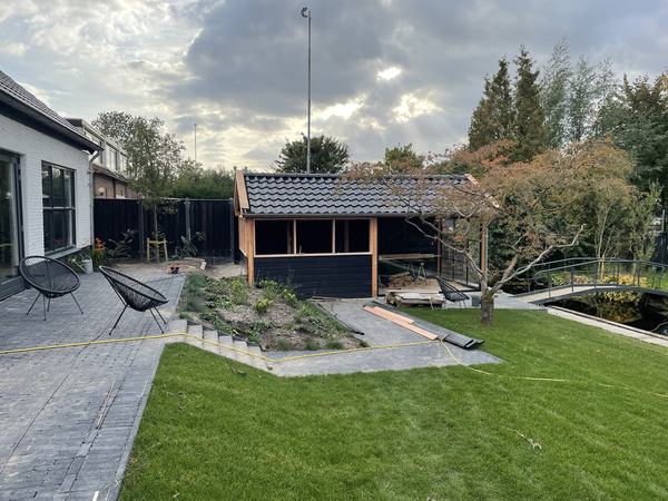 Dezelfde tuin na de aanleg met gazon, bestrating, trap en overkapping